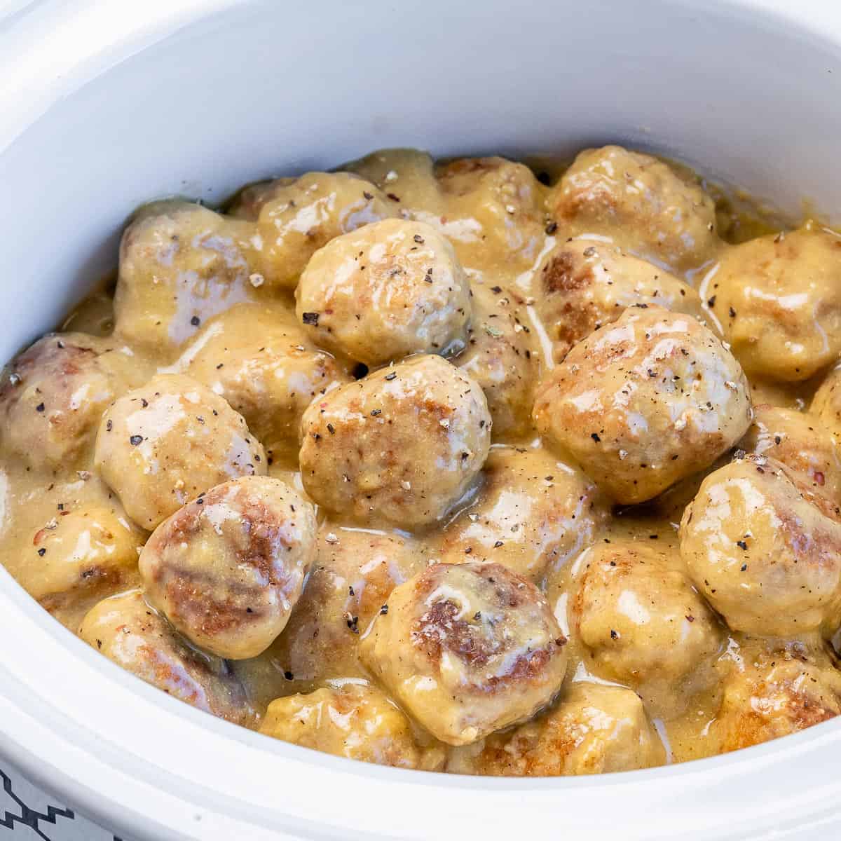 side close up shot of a white crockpot with creamy Swedish meatballs