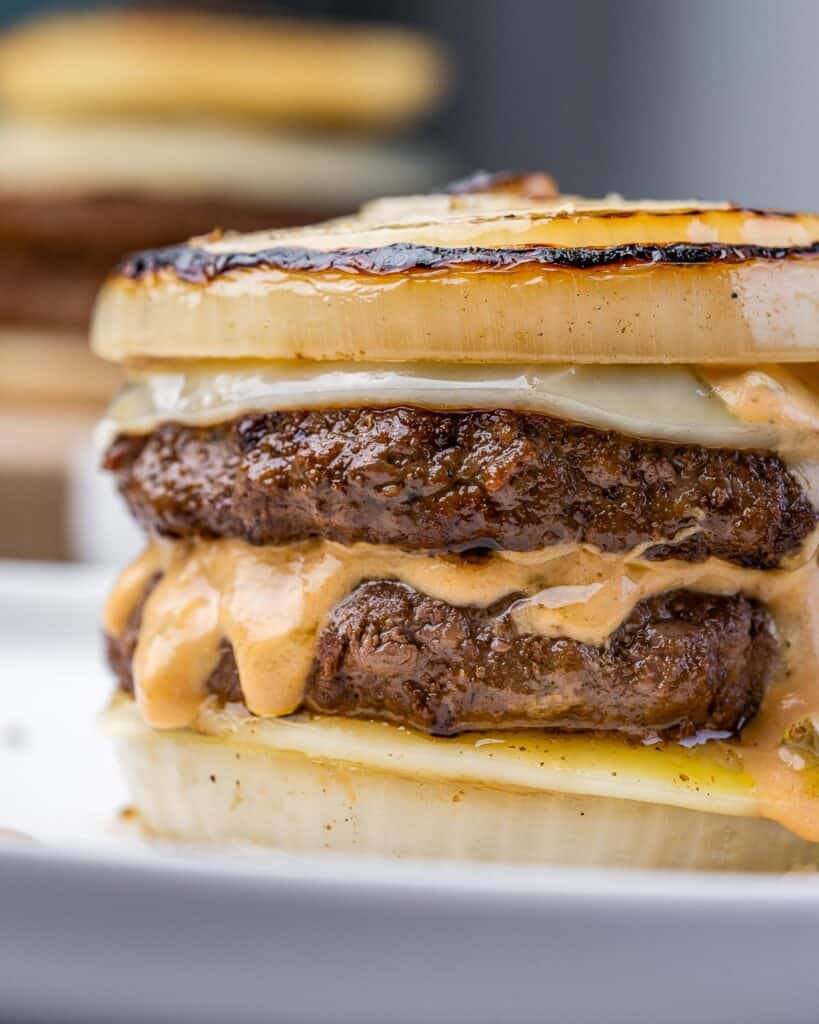 close up side shot of flying dutchman burger on a plate with sliced onion buns and melted cheese slices