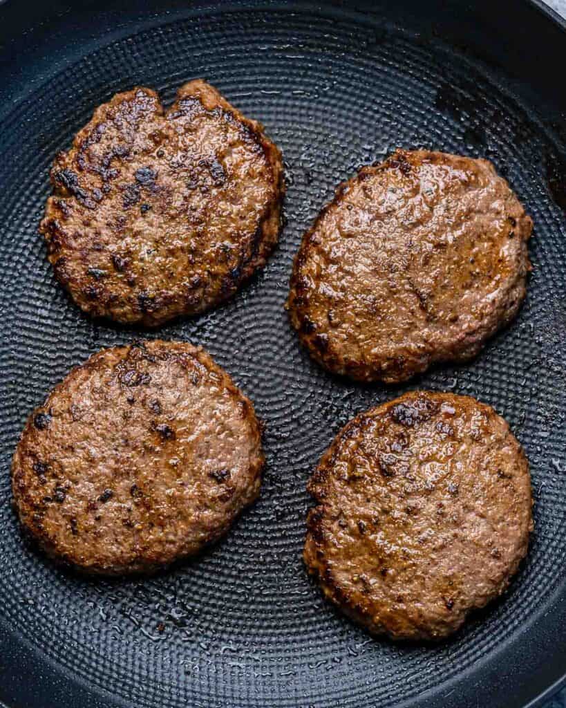4 burger patties cooked on a pan