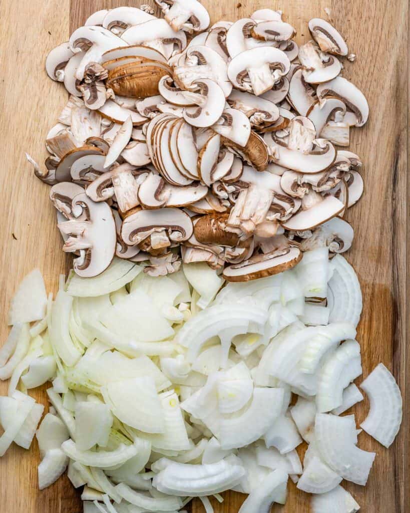 Chopped onion and mushrooms on a cutting board.