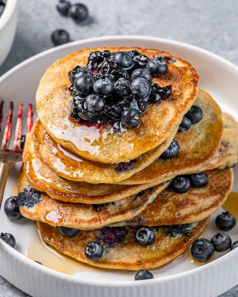Stack of lemon blueberry ricotta pancakes topped with syrup and fresh blueberries.