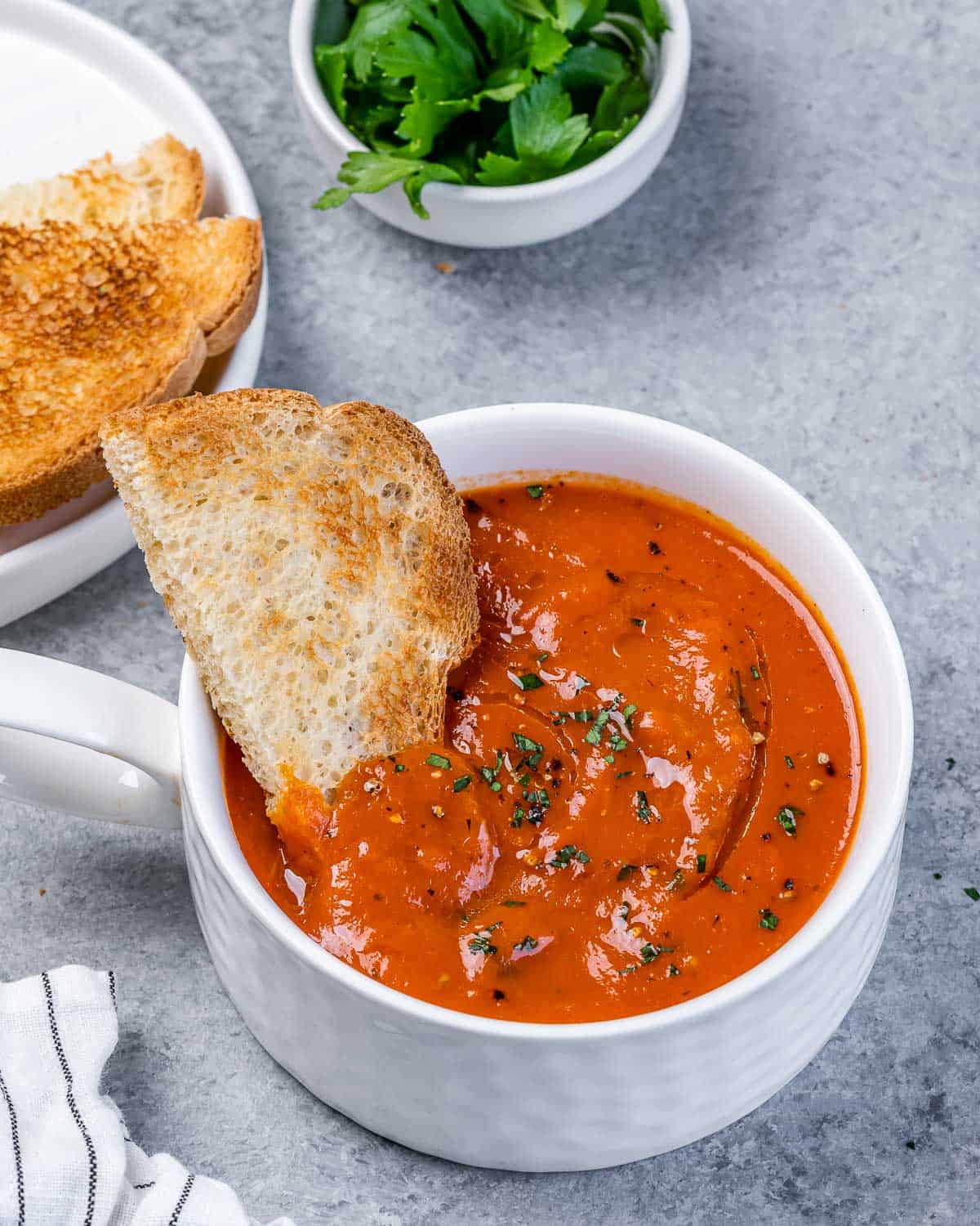 Piece of toast in a bowl of roasted red pepper soup.
