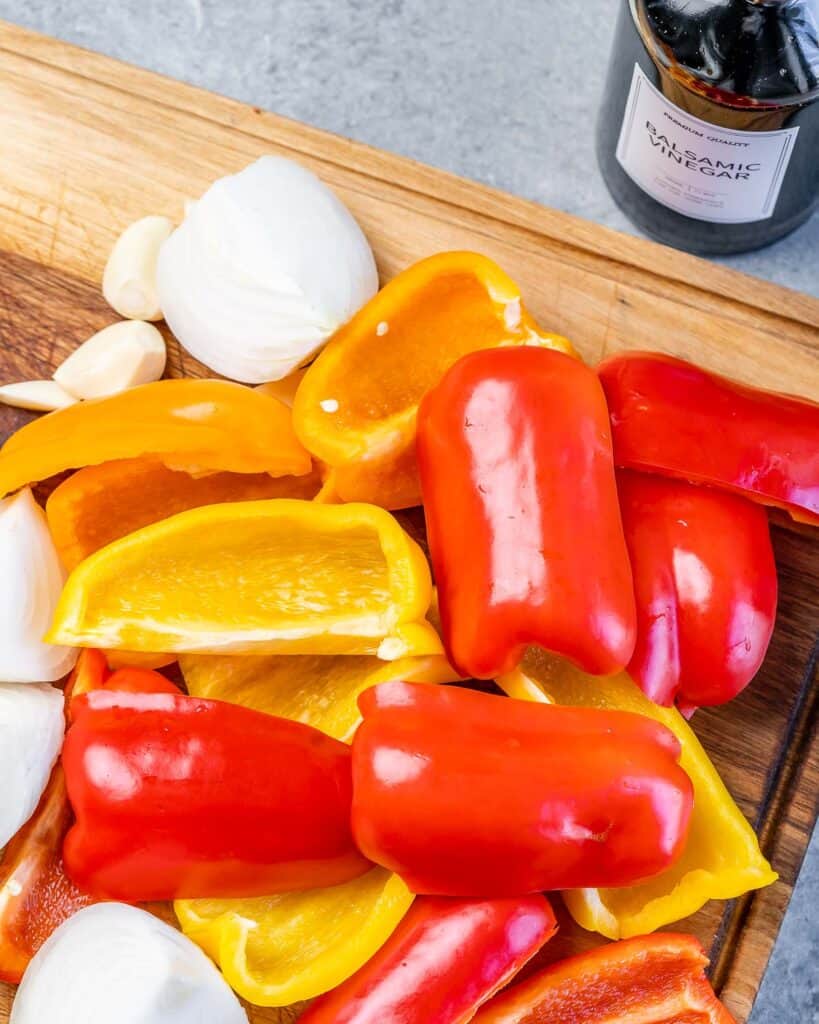 Red, yellow and orange bell peppers and onions chopped on a cutting board. 