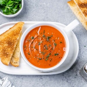 Top view of a small round white bowl of pepper soup on a plate with toast next to it.