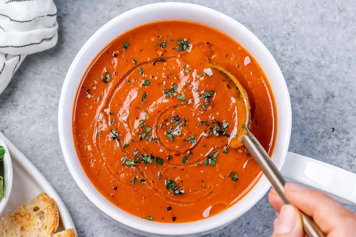Stirring a spoon in a bowl of roasted red pepper soup.