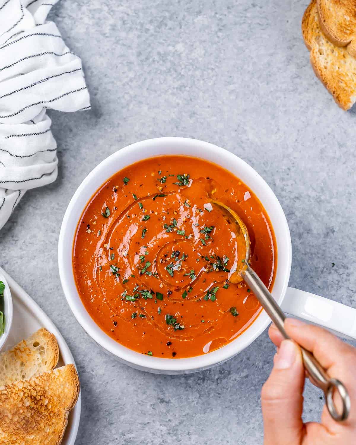 Stirring a spoon in a bowl of roasted red pepper soup.