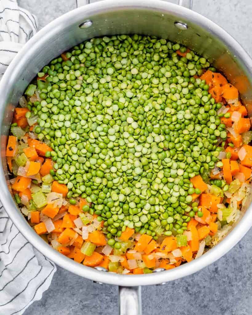 Adding peas to other veggies sautéing in a pot.