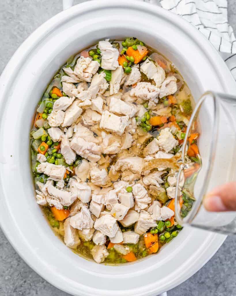 Adding broth to veggies and chicken in a slow cooker.