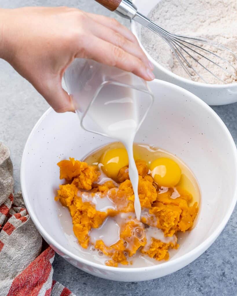Adding milk to a bowl with sweet potatoes and eggs.