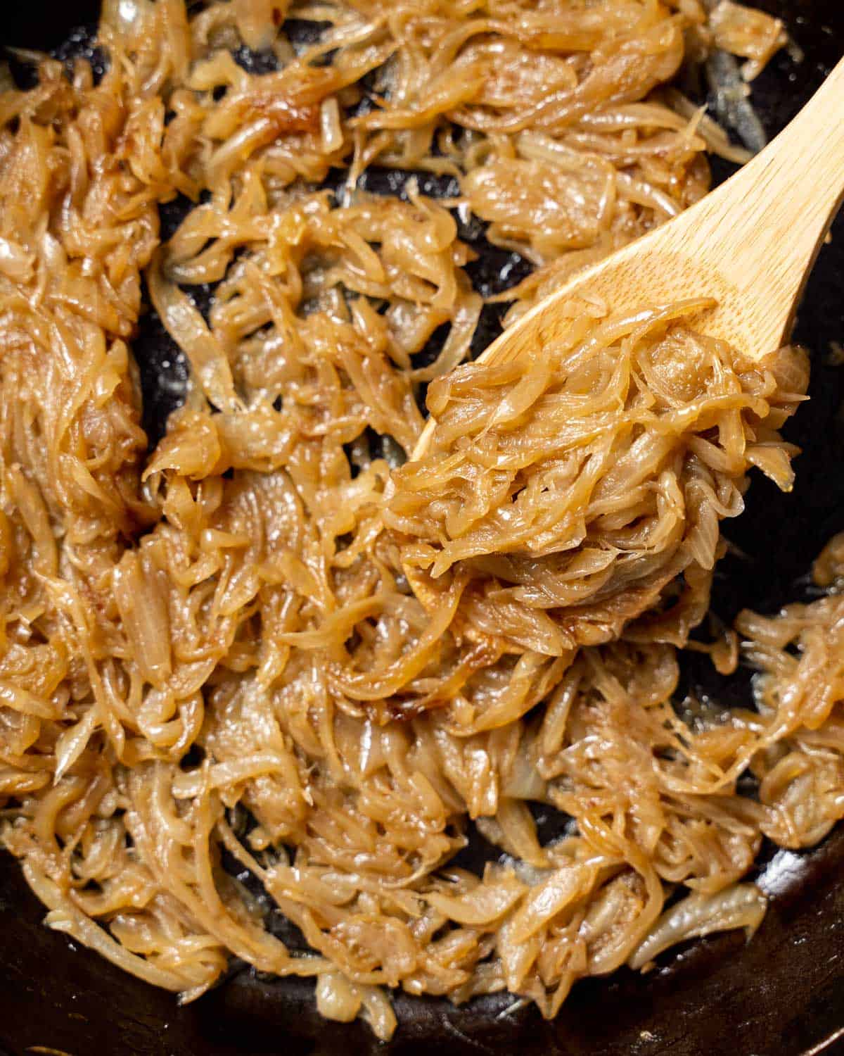 side shot of a skillet with sauteed caramelized onions with a wooden spoon in pan