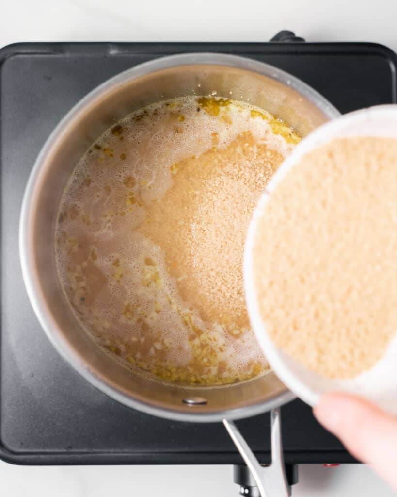 Adding couscous into boiling water in a pot.
