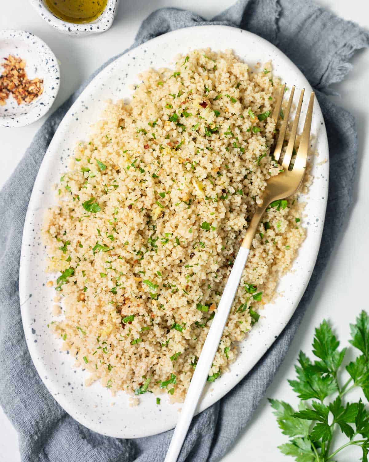 Couscous with fresh parsley on a white serving platter with a fork.