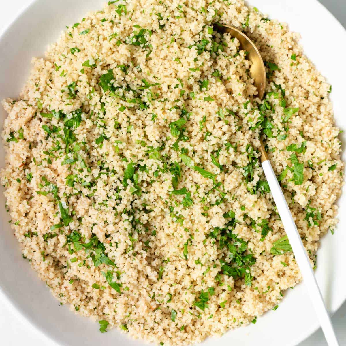 top view of a round plate of cooked couscous with chopped parsley and spoon on plate over couscous