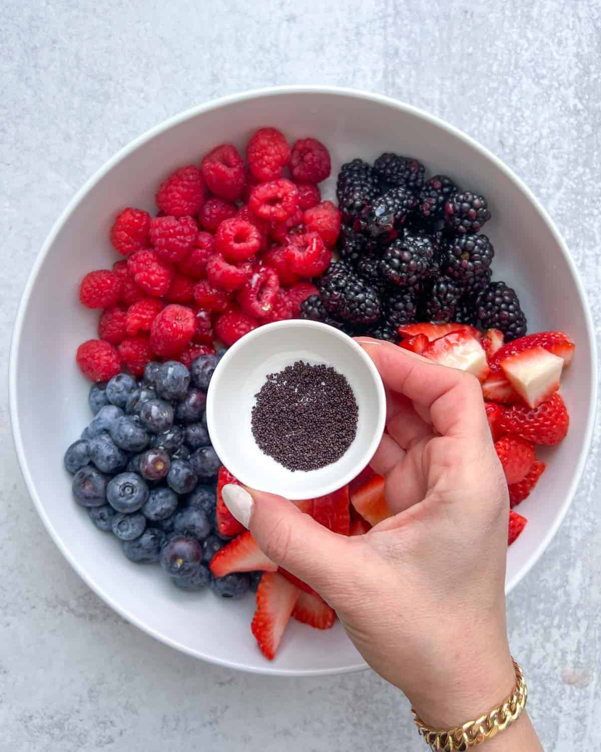 hand holding a small bowl of poppy seed over a bowl or berries.