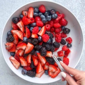 hand mixing the berry salad using a spoon.