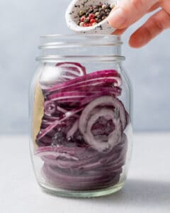 adding peppercorns in the jar with the sliced red onions.