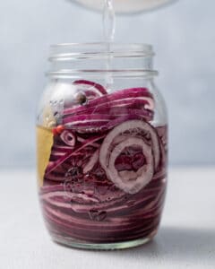 adding the brine into the jar with onions.