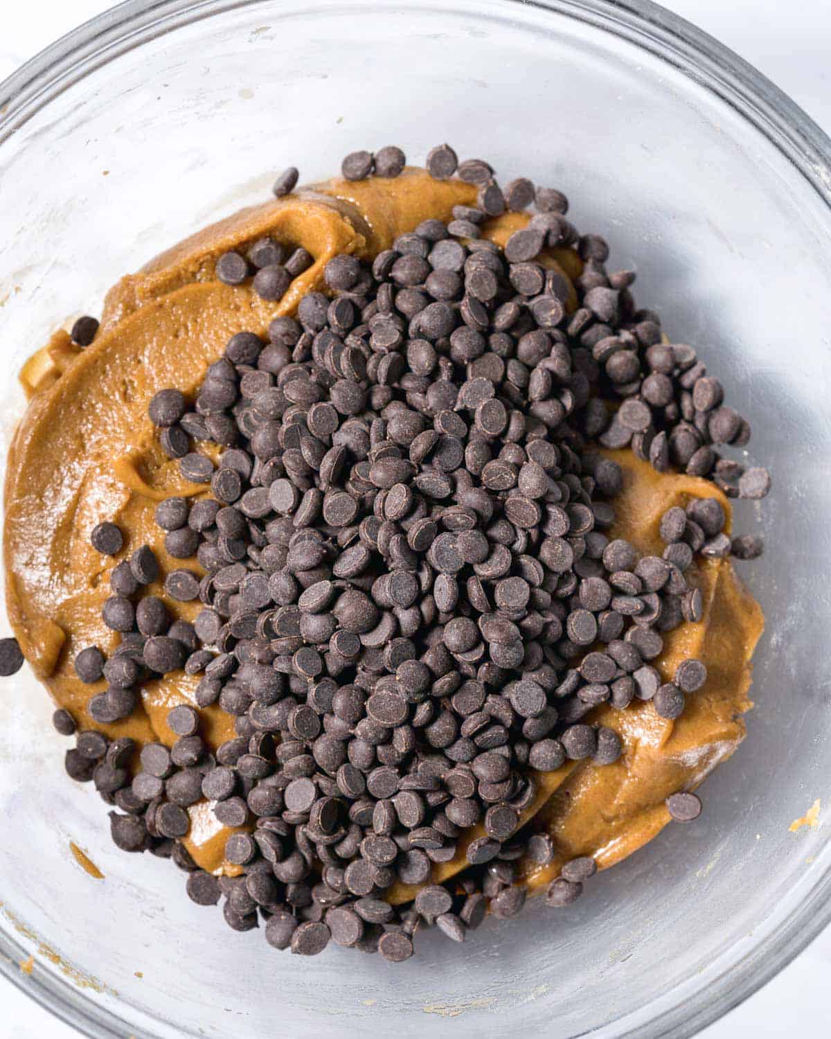 chocolate chips added over cookie dough in a bowl.
