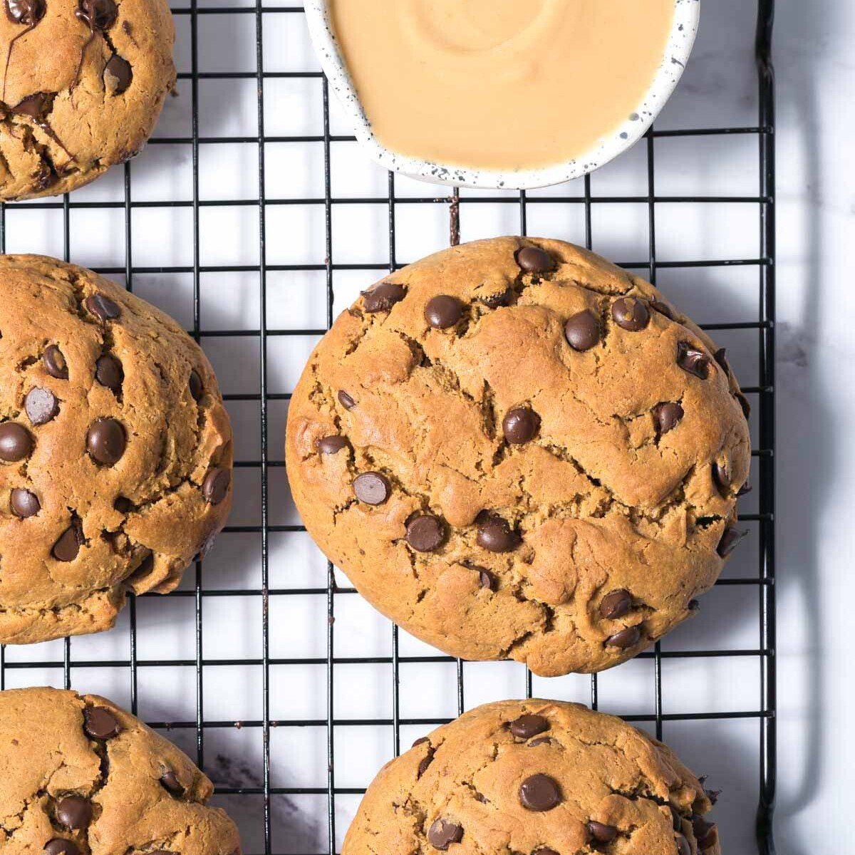 a wire rack with chocolate chip cookies next to a small bowl with melted peanut butter.