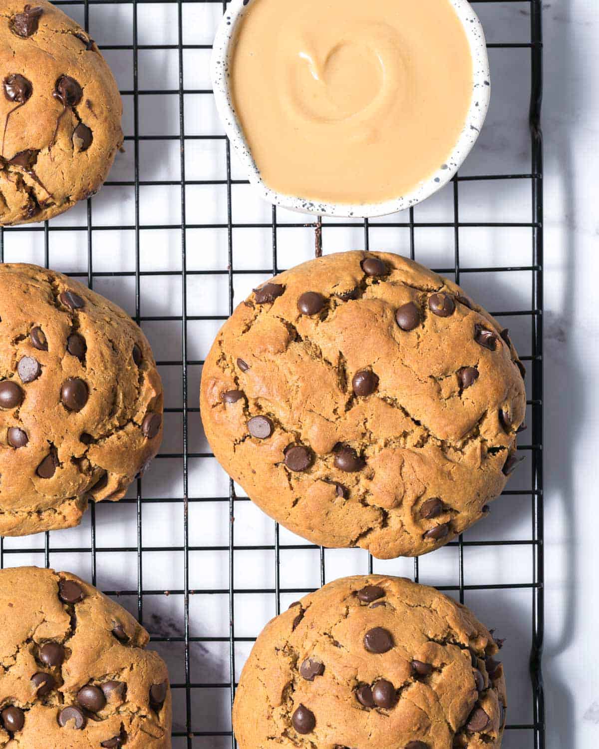 a wire rack with chocolate chip cookies next to a small bowl with melted peanut butter.