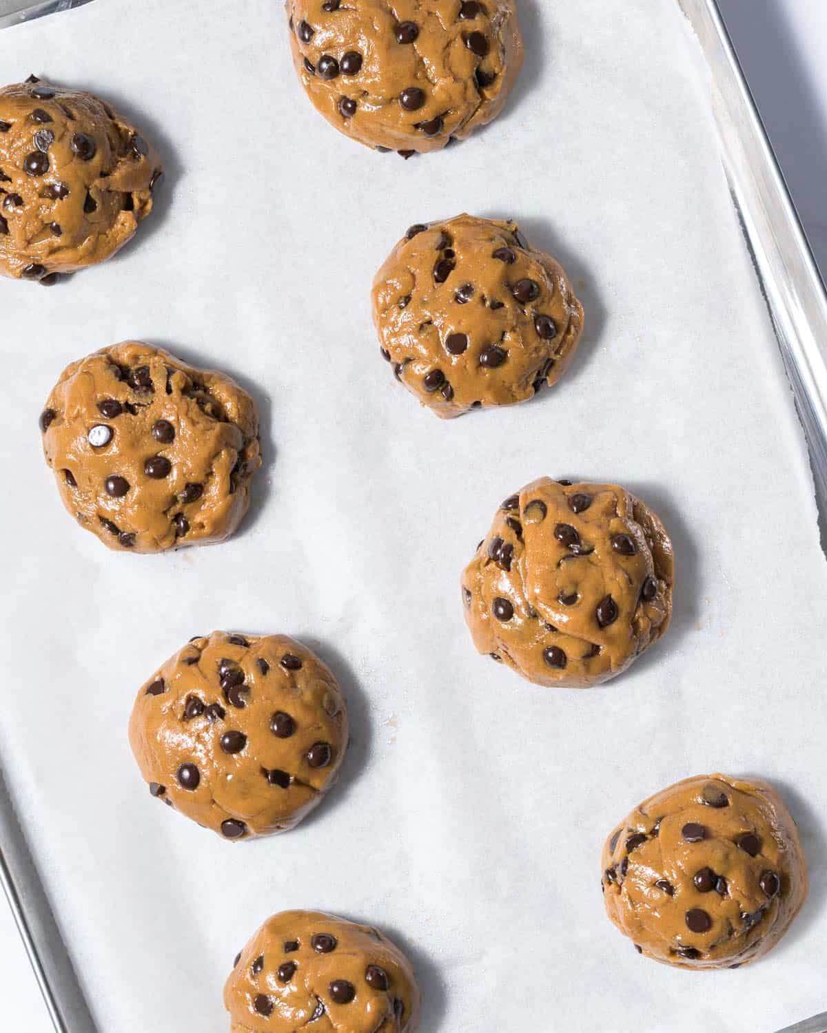 cookie dough balls in a sheet pan with parchment paper before baking.