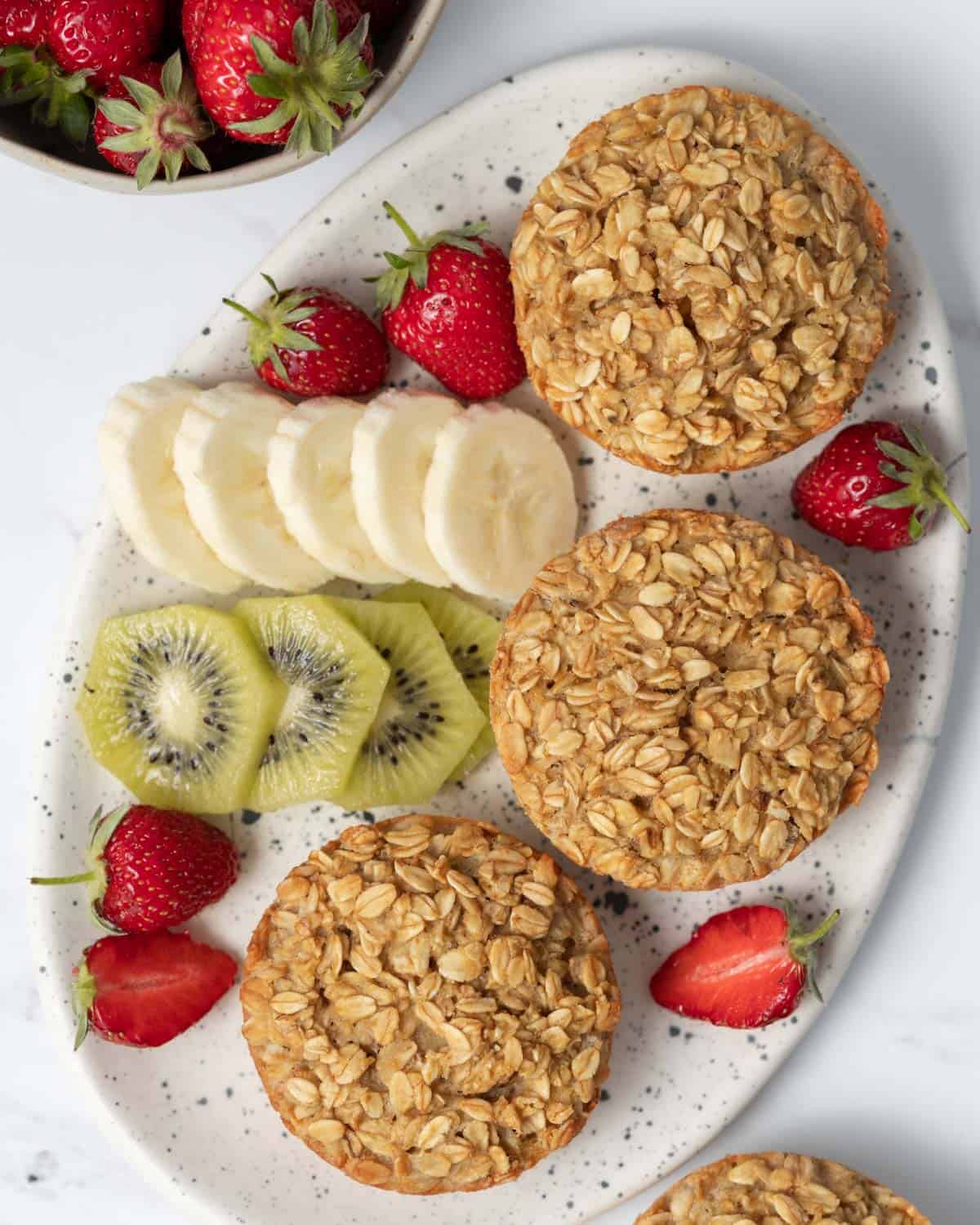 3 protein muffins on a plate with a side of sliced fruits.