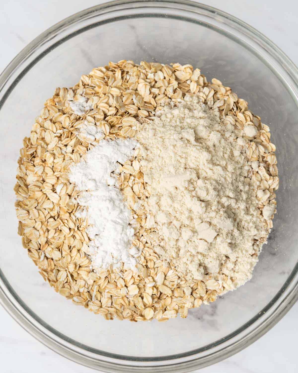 oats, baking powder, and protein powder are added to a round bowl.