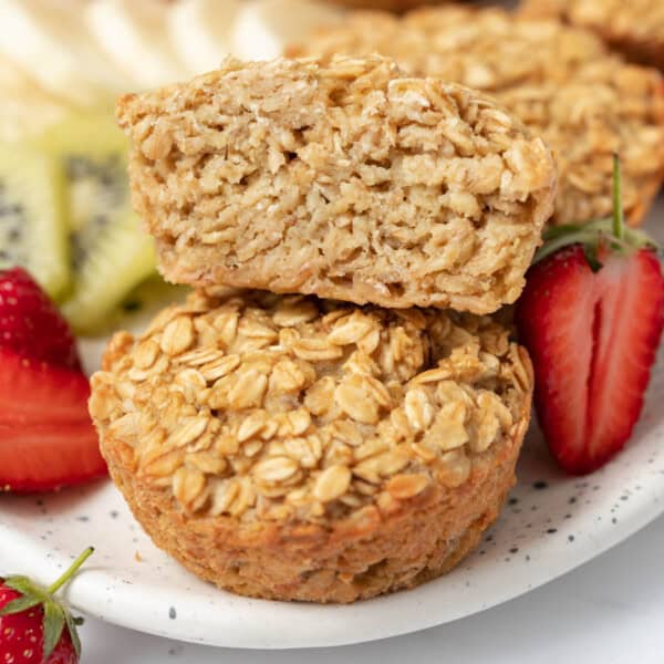 one-half muffin over another whole muffin on a plate with sliced fruits.