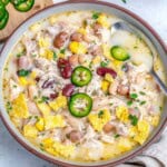 a bowl with white chicken chili made with 4 different beans and a spoon in the bowl.