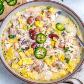 a bowl with white chicken chili made with 4 different beans and a spoon in the bowl.