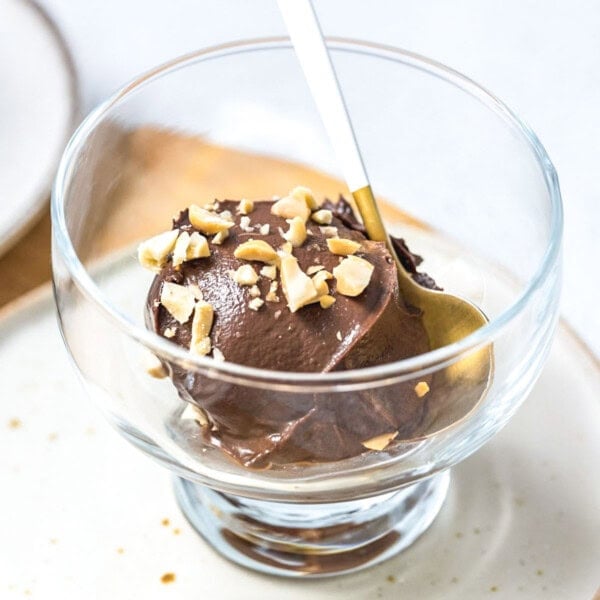 a clear bowl with avocado ice cream topped with chopped peanuts.