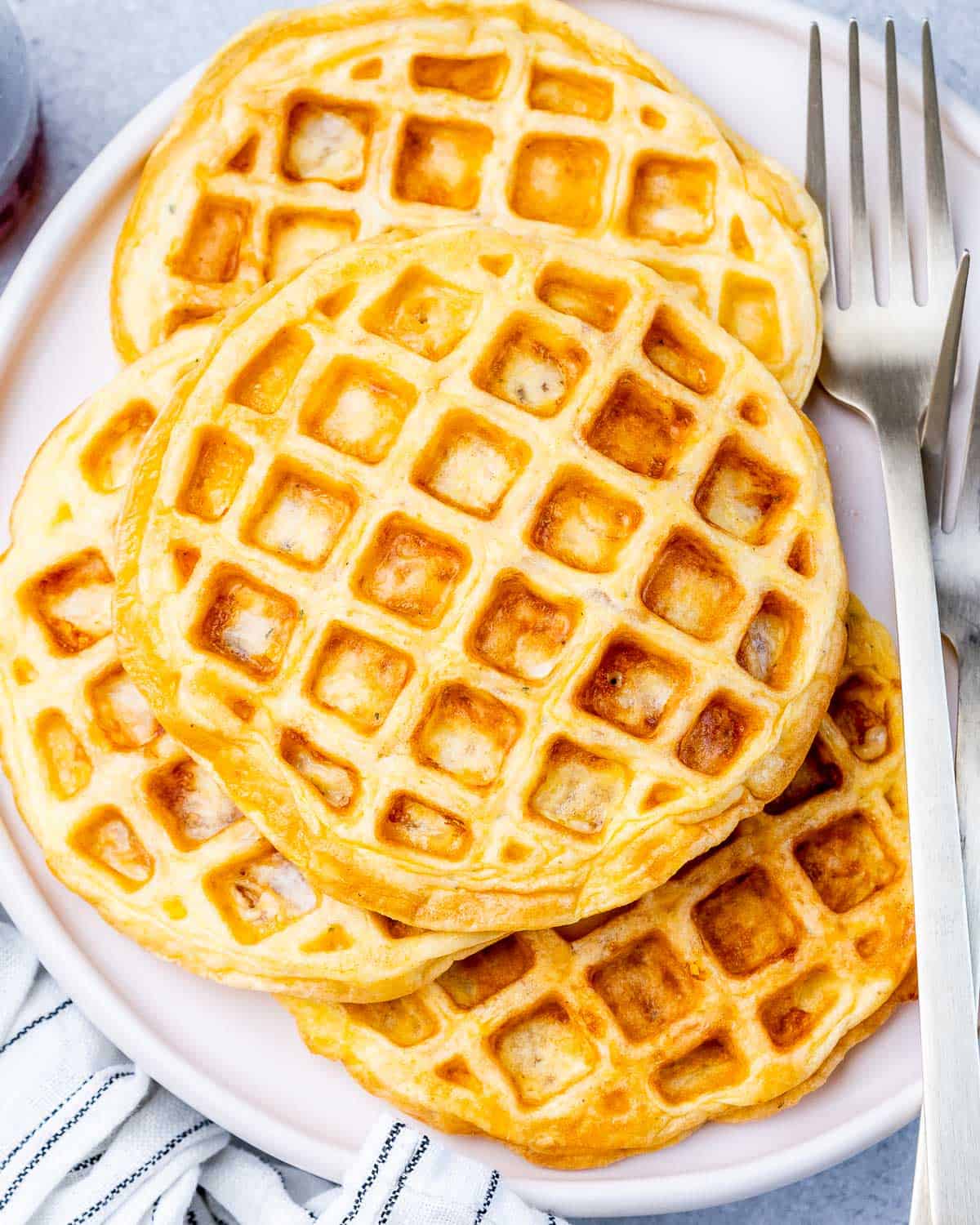 A stack of three golden-brown chaffles on a white plate with a fork on the side, ready to serve.