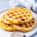 A plate with four chaffles piled high, lightly overlapping, with a gray napkin and silver fork nearby.
