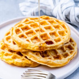 A plate with four chaffles piled high, lightly overlapping, with a gray napkin and silver fork nearby.