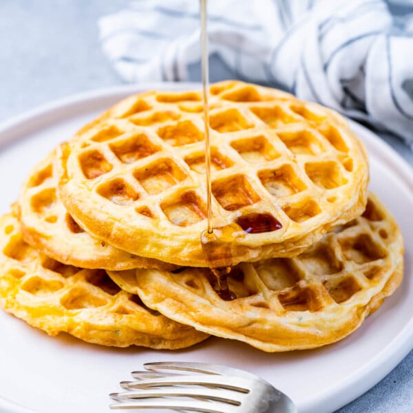 A plate with four chaffles piled high, lightly overlapping, with a gray napkin and silver fork nearby.