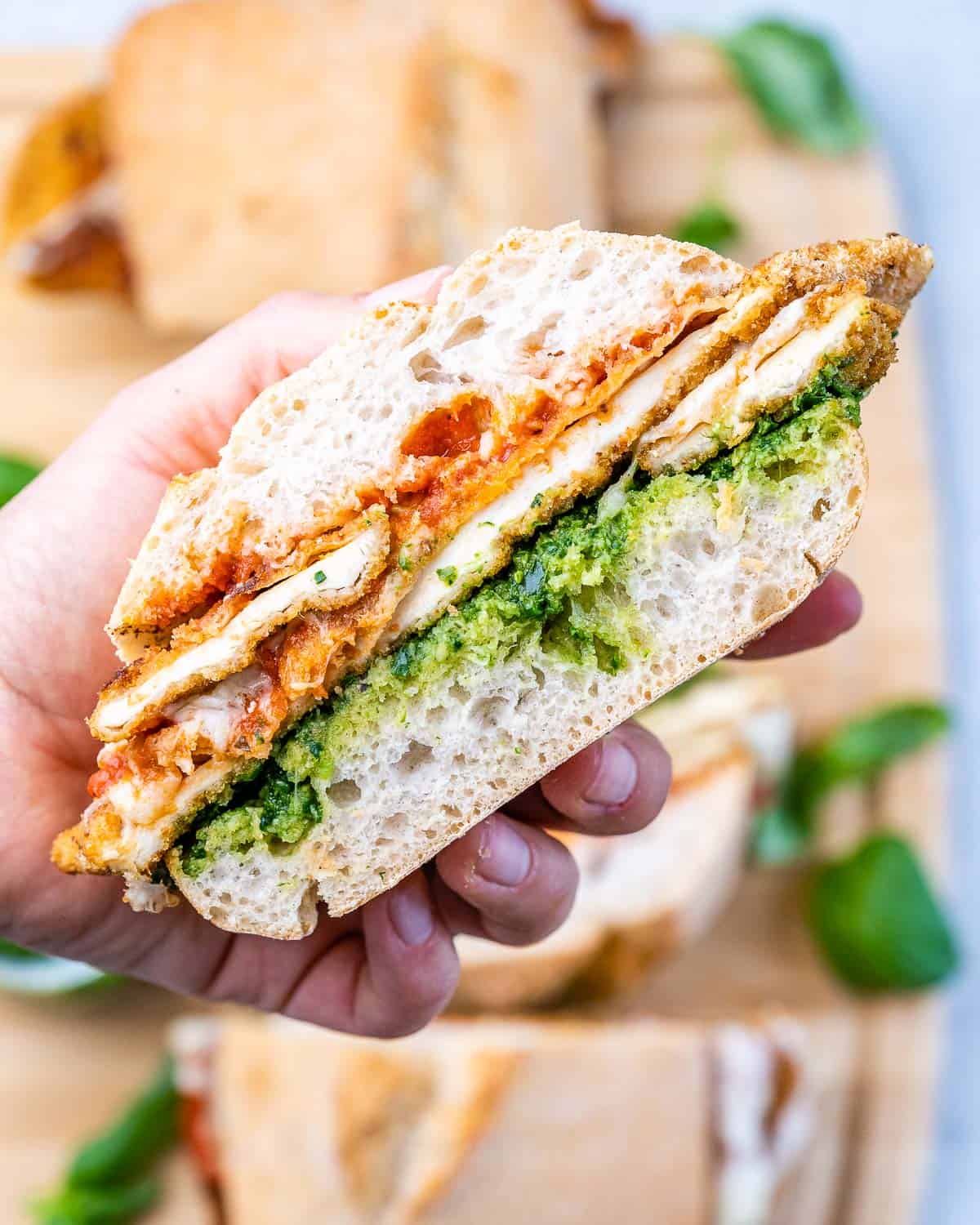 Another hand-held shot of the sandwich with breaded chicken and pesto clearly visible between the toasted bread layers.