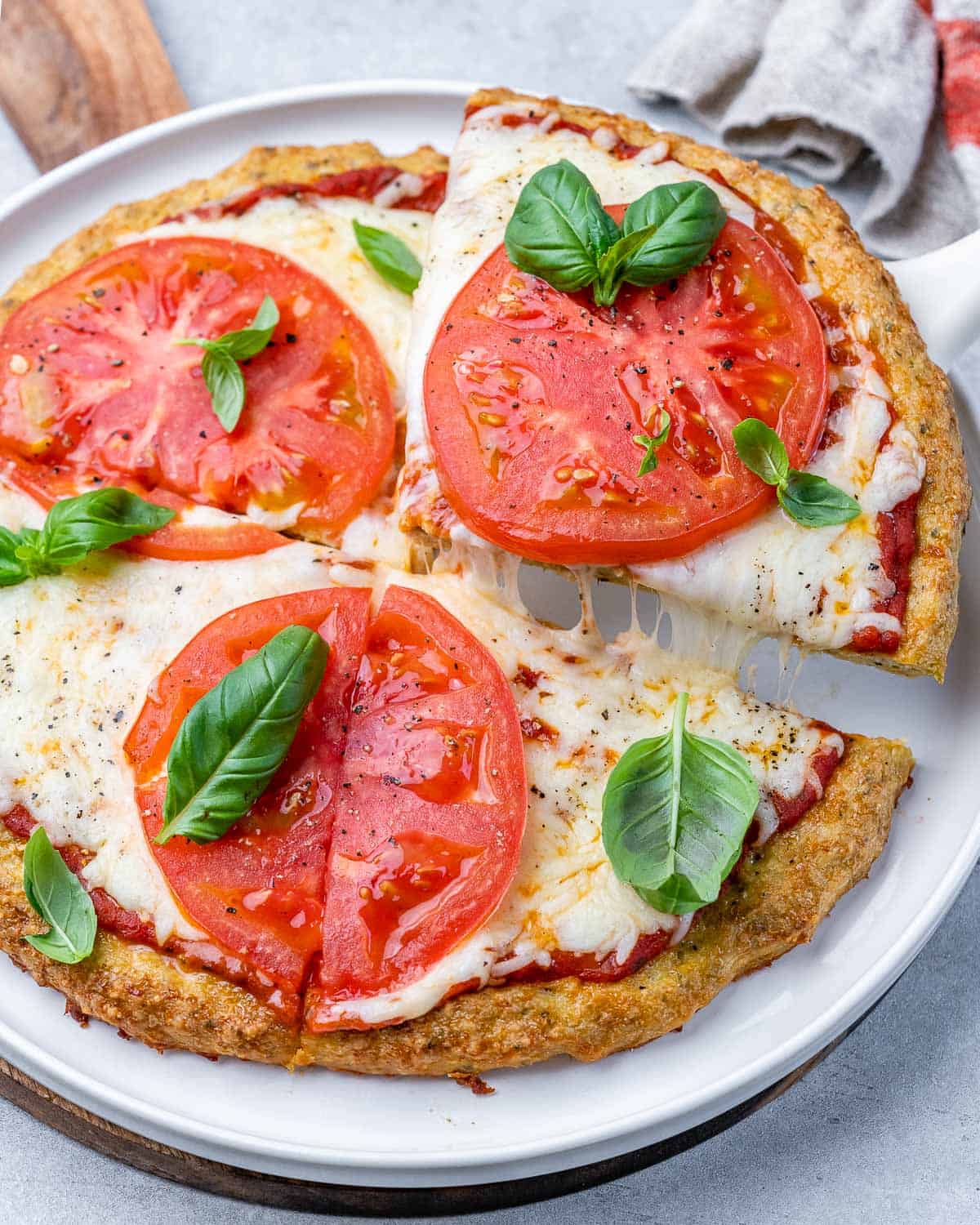 Chicken crust pizza topped with sliced tomato on a white plate.