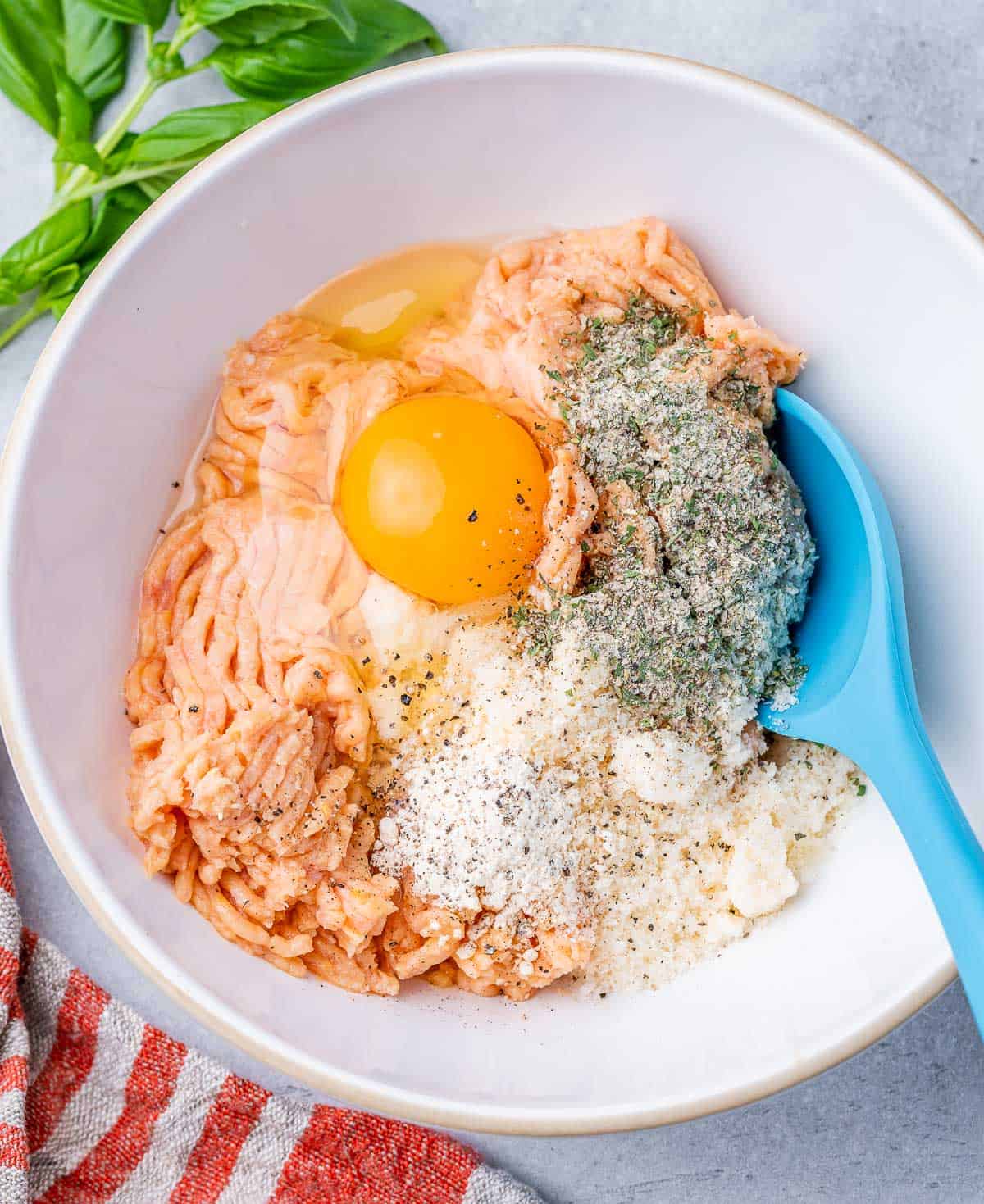 Mixing egg with ground chicken and seasonings in a white bowl.