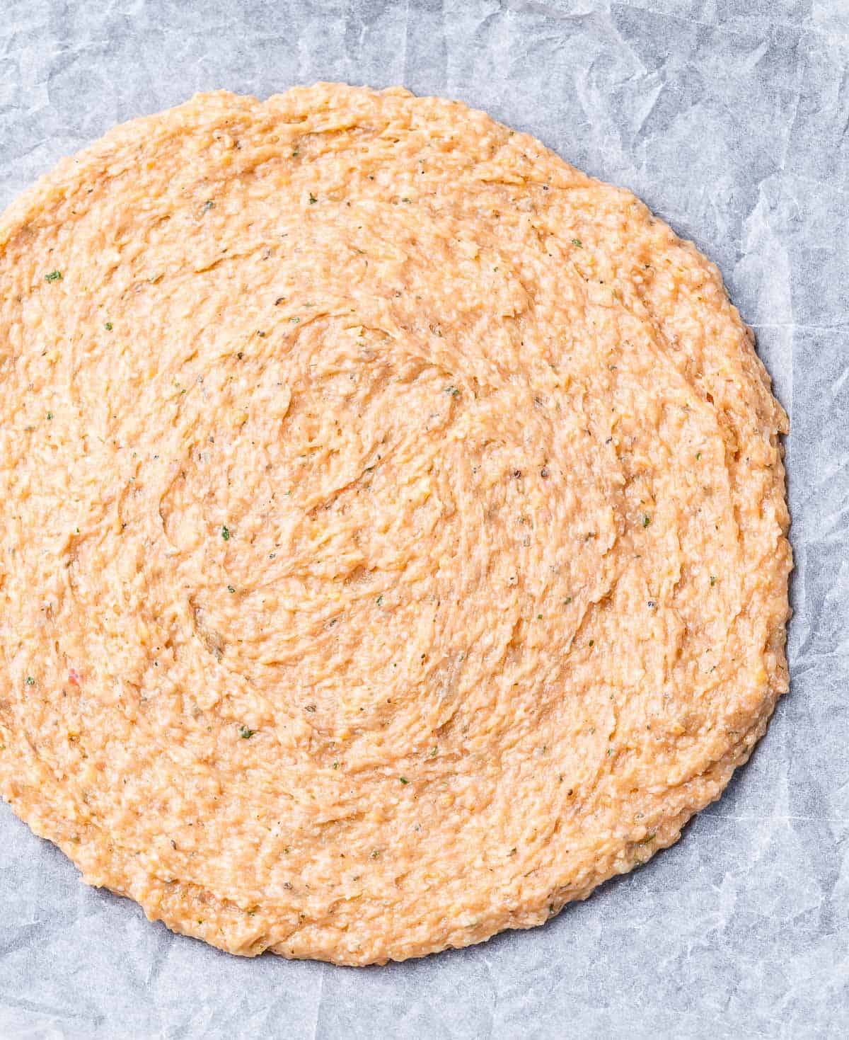 Pizza dough on a pan with parchment paper.