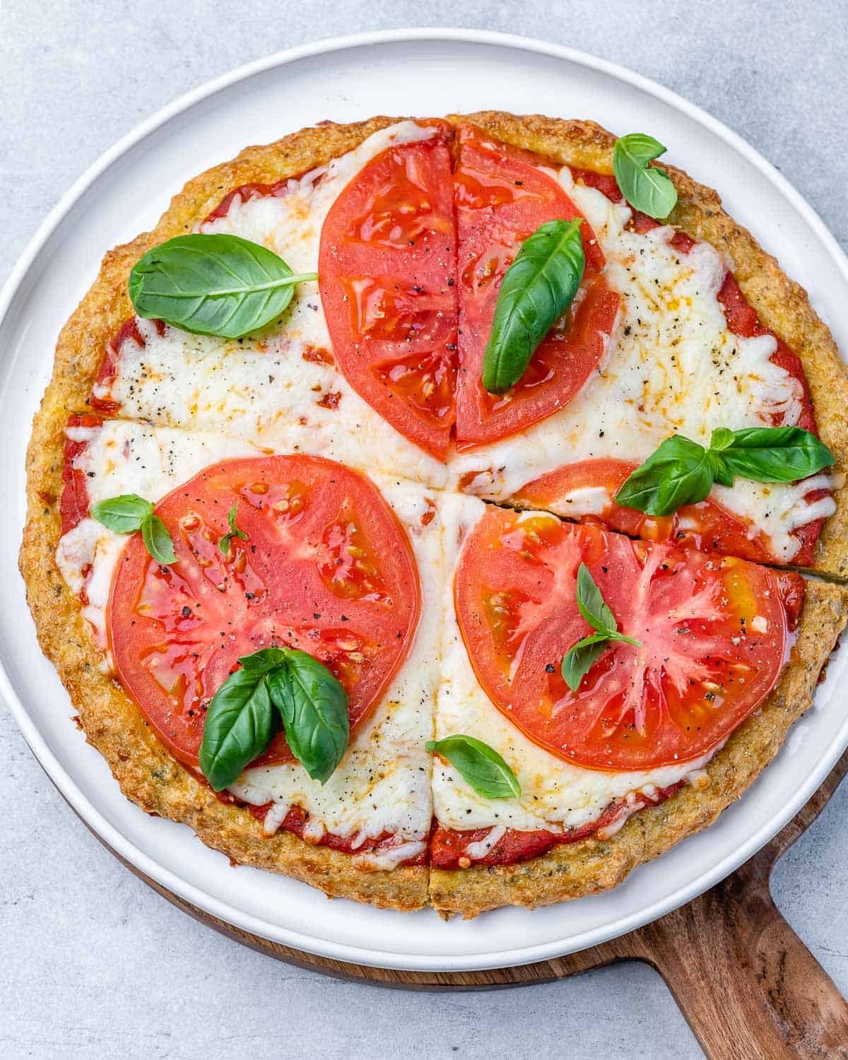 Chicken crust pizza topped with cheese, tomato slices and fresh basil on a white plate.