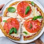 chicken crusted pizza with melted cheese and sliced red tomatoes, garnished with fresh basil leaves.