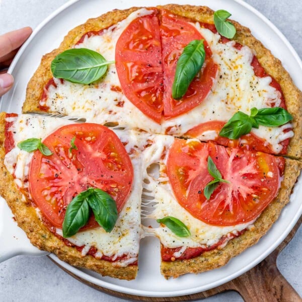 chicken crusted pizza with melted cheese and sliced red tomatoes, garnished with fresh basil leaves.