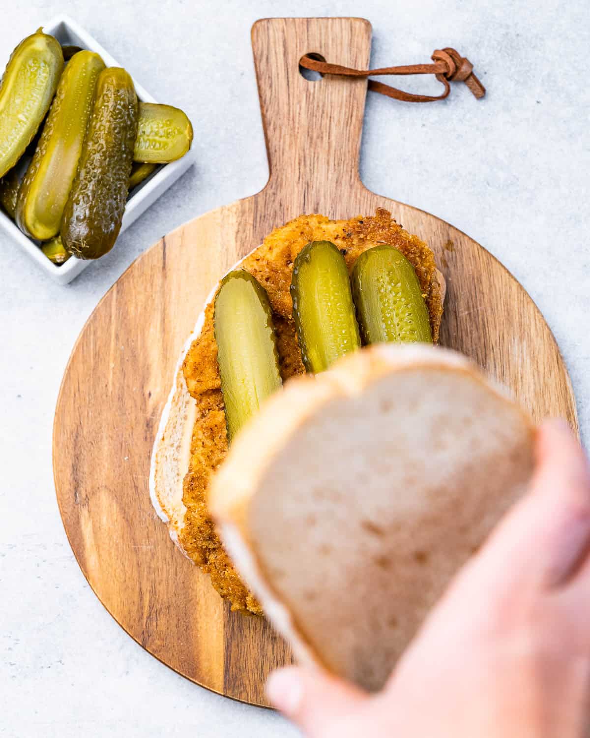 Assembling a sandwich with chicken and pickles.