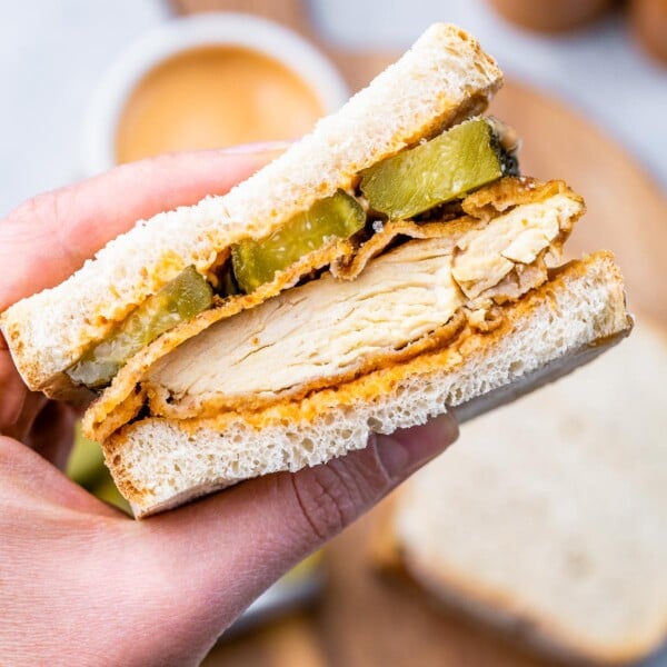 chicken cutlet sandwich cut in half with a hand holding it.