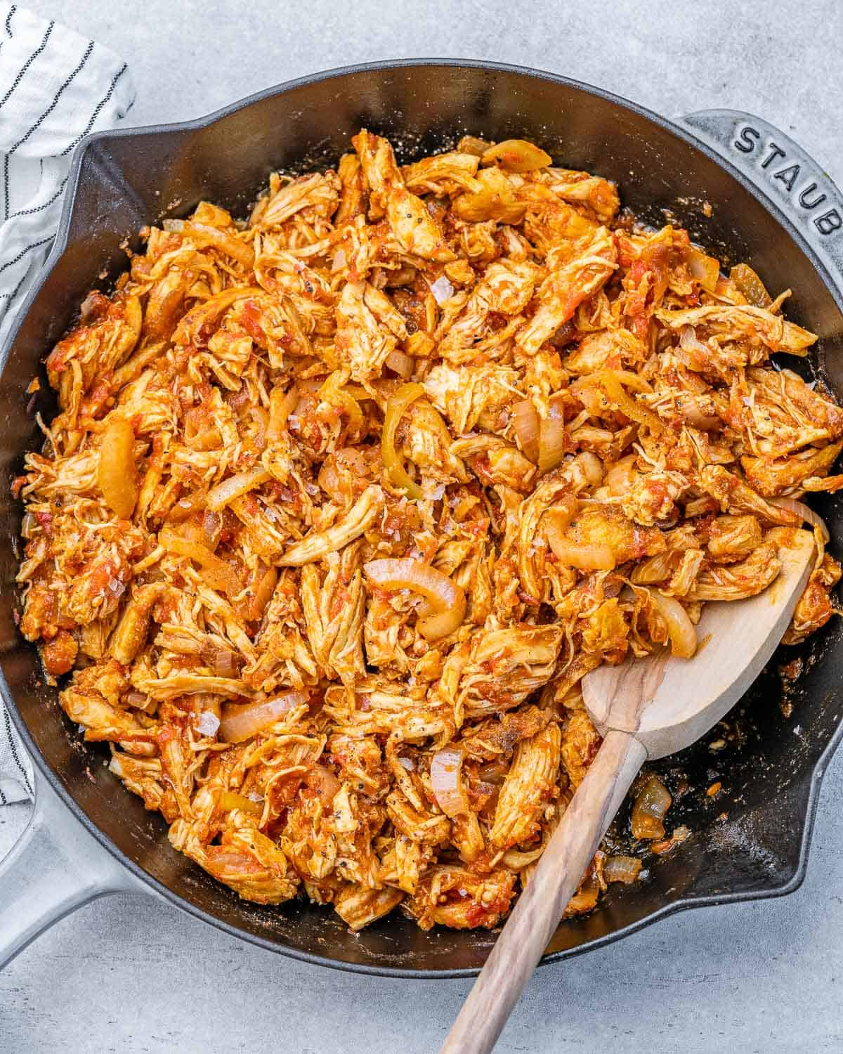 Stirring saucy shredded chicken in a skillet with a wooden spoon.