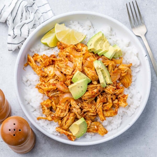 shredded cooked chicken that's orange-looking with chopped avocado garnishes.