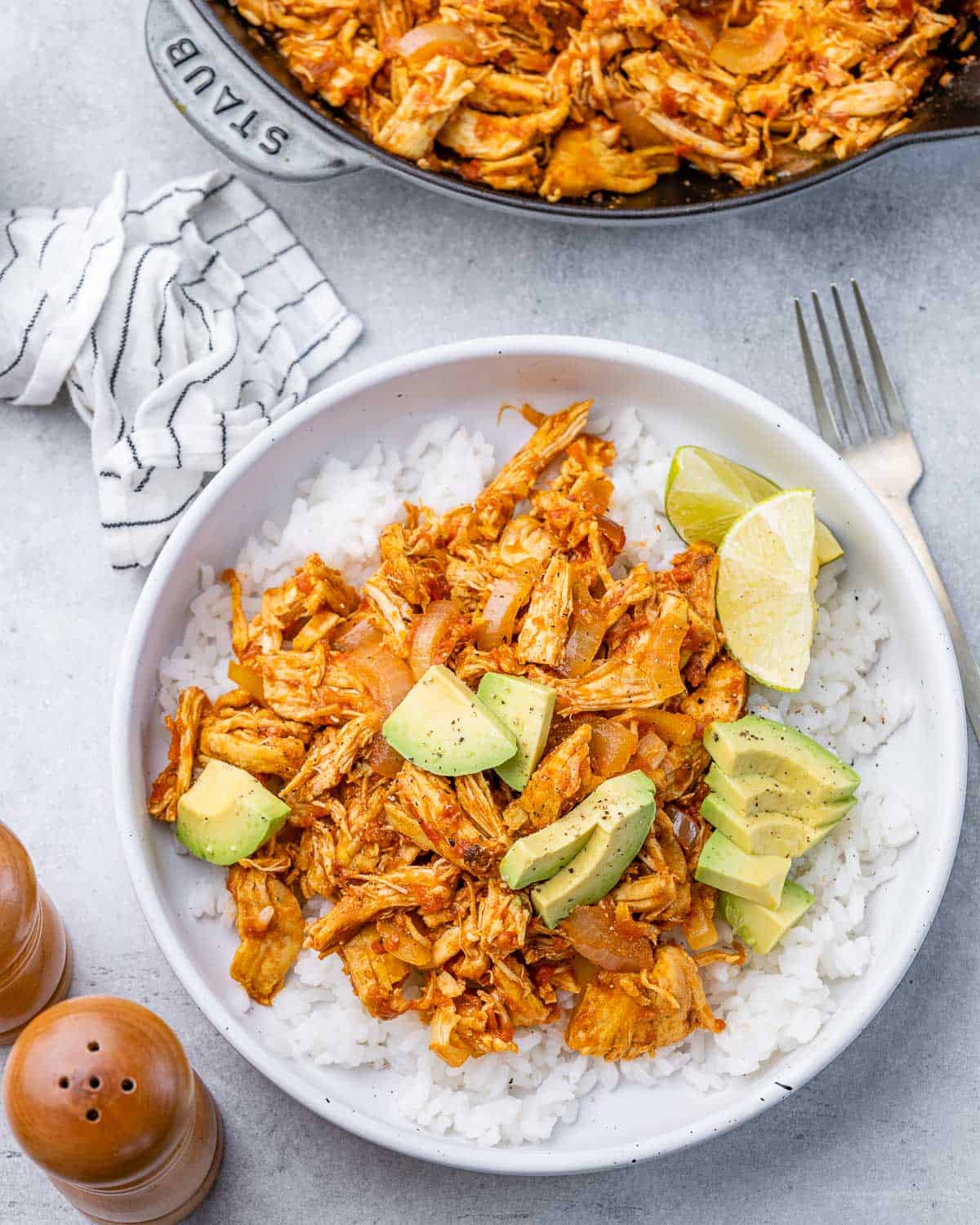Chicken Tinga served with rice, fresh lime wedges and avocado in a white bowl.