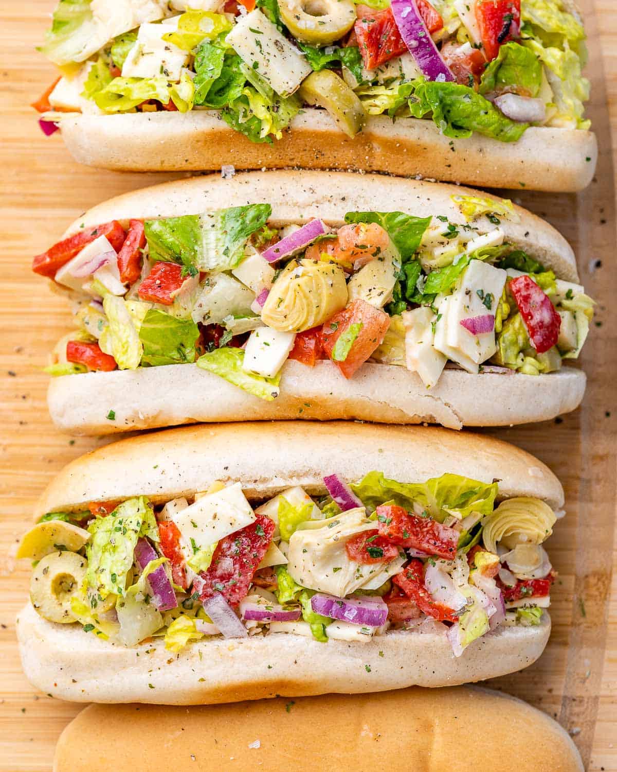 3 buns on a cutting board filled with chopped salad.