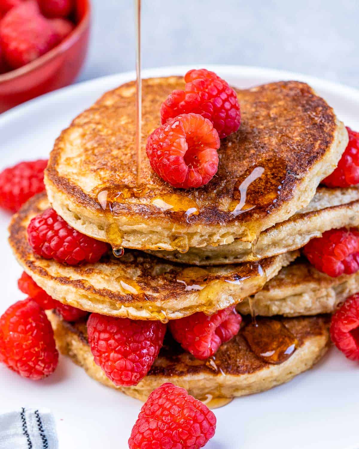 stacks of pancakes on a plate topped with raspberries with a drizzle of maple syrup