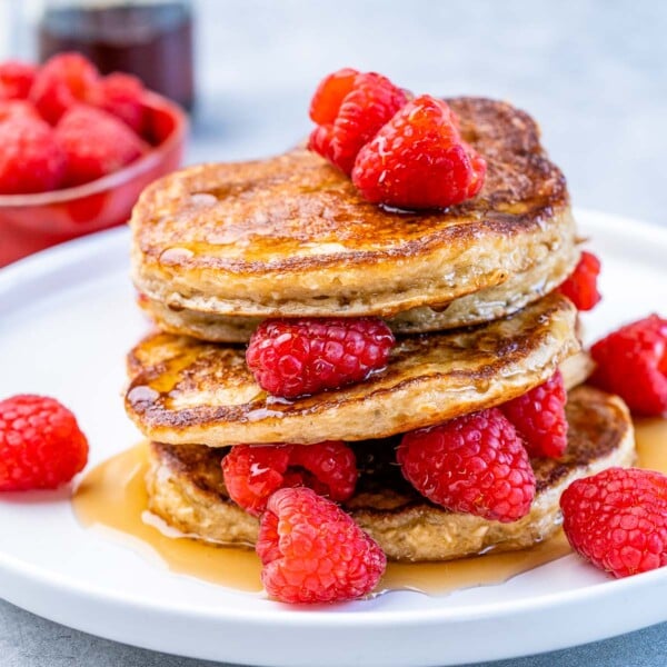 Side shot of stacks of pancakes with fresh raspberries and maple syrup drizzles.